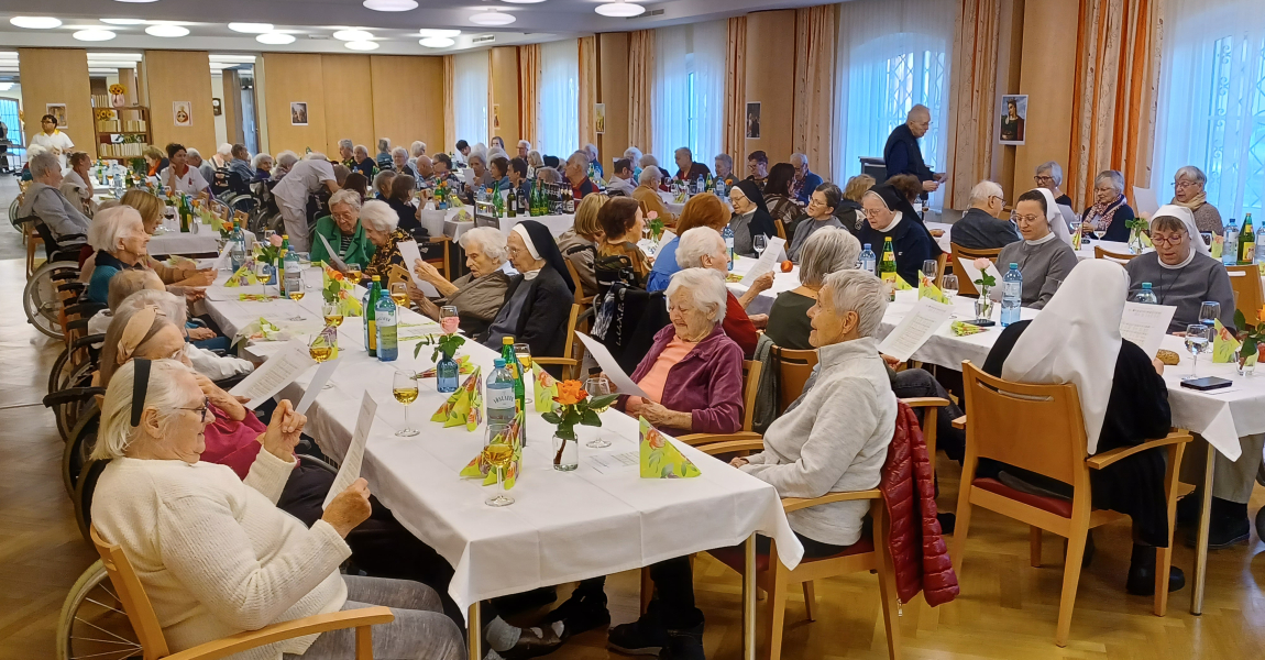 Veranstaltungssaal mit vielen BewohnerInnen welche bei den Tischen sitzen.